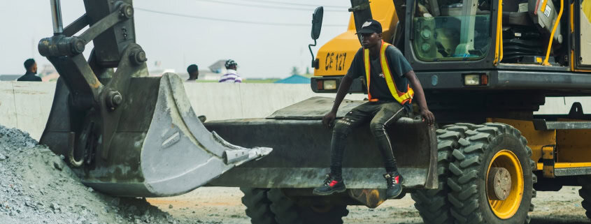 man in yellow and black jacket standing beside black and yellow heavy equipment